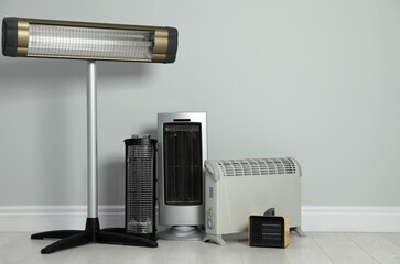 Different electric heaters near light grey wall indoors. Space for text