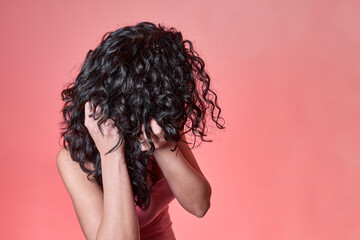 young black curly haired woman combing her hair following curly girl method on pink background....