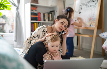 Mother working with small daughters in bedroom, home office concept.