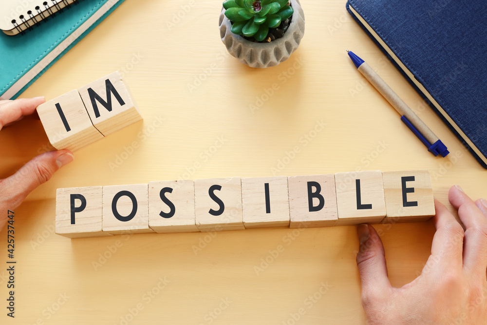 Poster man hand holding wooden cubes with the text impossible, removing the word im so it written possible.