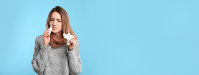 Naklejka na ściany i meble Sick young woman using nasal spray on light blue background