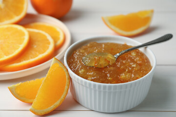 Fototapeta na wymiar Delicious orange marmalade in bowl with spoon on white wooden table