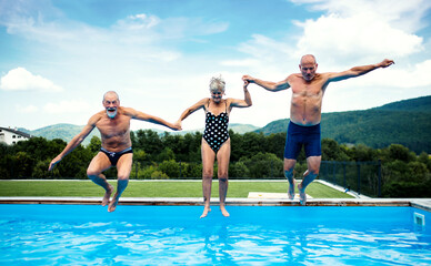 Group of cheerful seniors in swimming pool outdoors in backyard, jumping.