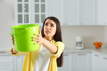 Young woman collecting leaking water from ceiling in kitchen, space for text. Time to call roof repair service