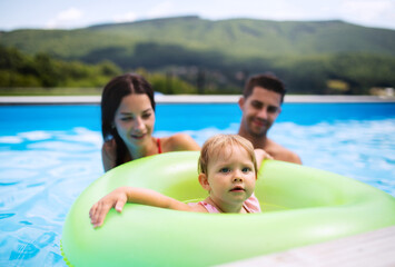 Fototapeta na wymiar Young family with small daughter in swimming pool outdoors in backyard garden.