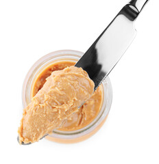 Glass jar and knife with tasty peanut butter on white background, top view