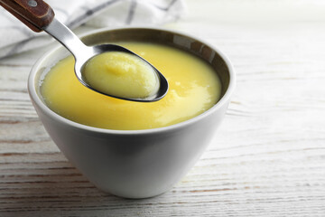 Bowl and spoon of Ghee butter on white wooden table, closeup