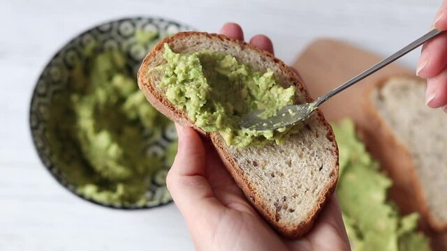 Spreading guacamole on whole grain bread, making a vegan healthy breakfast