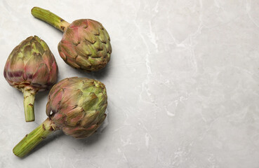 Obraz premium Fresh raw artichokes on grey marble table, flat lay. Space for text