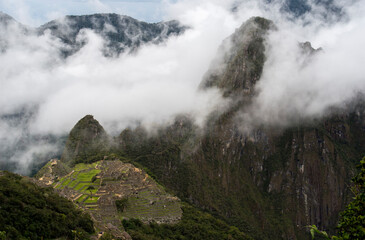 Steep mountains of Peru with low clouds and remains of ancient city below 