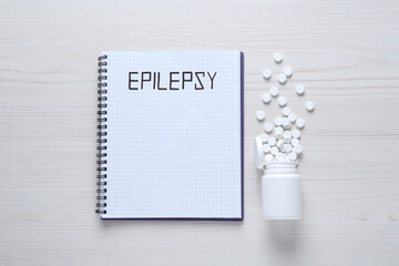 Notebook with word Epilepsy and pills on white wooden table, flat lay