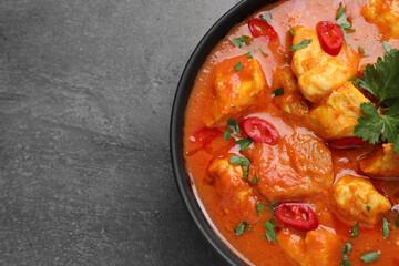 Bowl of delicious chicken curry on grey table, top view. Space for text