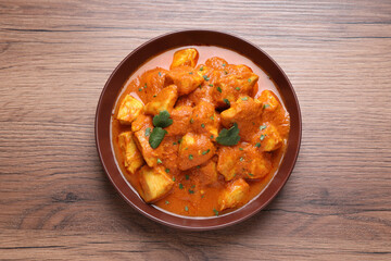 Bowl of delicious chicken curry on wooden table, top view