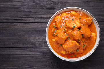 Bowl of delicious chicken curry on black wooden table, top view. Space for text