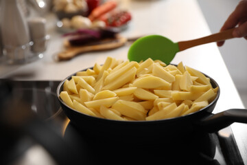Man stirring cut raw potatoes in frying pan, closeup