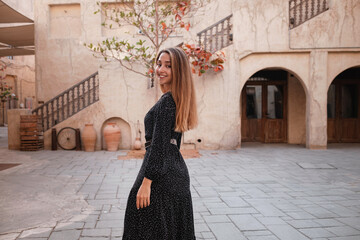 Happy woman traveler wearing black dress walking through the streets - 425743463