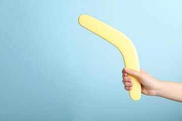 Woman holding boomerang on light blue background, closeup. Space for text