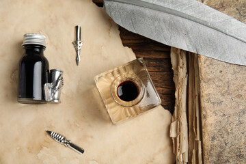Feather pen, inkwell and paper on wooden table, flat lay