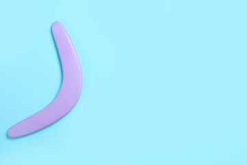 Lilac wooden boomerang on light blue background, top view. Space for text - obrazy, fototapety, plakaty