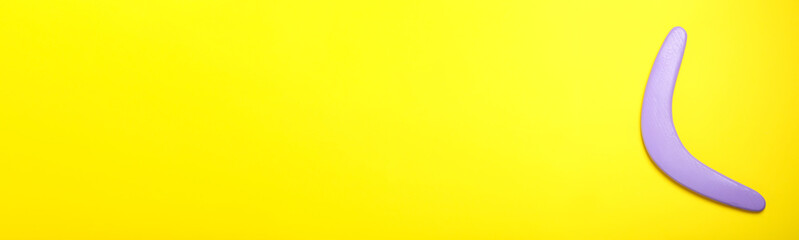 Lilac boomerang on yellow background, top view. Space for text
