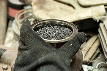 A hand in a black mitten holds a jar of nails.