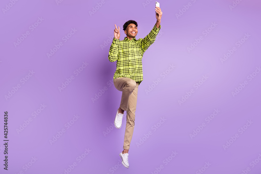 Sticker Full length body size of young jumping high taking selfie showing v-sign smiling isolated on pastel purple color background