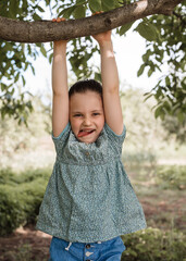 A little girl climbs a tree in the garden. Summer fun in nature