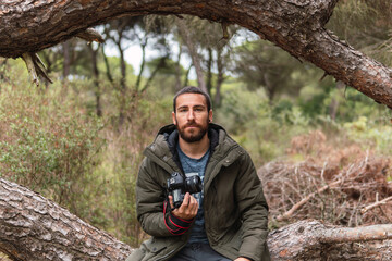 Professional photographer sitting in a tree with his camera in his hand looking straight ahead.