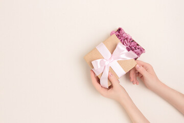 Female hands open a gift box with a tied bow with eustoma flowers inside. Congratulation concept on a beige background. Giving present for springtime holidays.