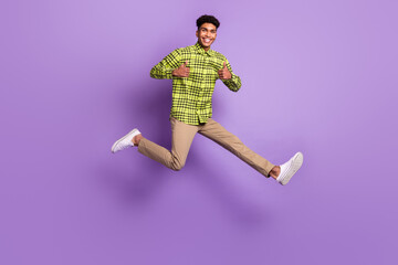 Full size photo of brunette dark skin man jump up show thumbs up wear casual clothes isolated on violet color background