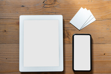 Selected objects arranged on a wooden work table: smartphone tablets with empty display and white business cards to fill with the company or brand graphics - Mockup business