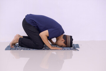 Side view of asian muslim man doing Salat with prostration pose on the prayer mat