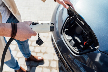 Man inserts plug of the charger into the socket of electric car close-up