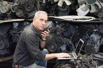 Engineer man working, Caucasian manager with no helmet using laptop, walkie-talkie and looking at auto part in factory-warehouse