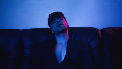 man in blazer looking at camera and sitting on sofa on blue