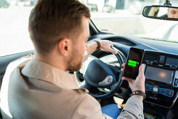 Man watching electric car charge indicator through smartphone app. Battery level on the mobile phone screen