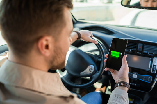 Man watching electric car charge indicator through smartphone app. Battery level on the mobile phone screen
