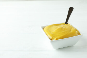 Bowl with mustard and spoon on white wooden table