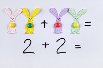 Teaching children the basics of addition of mathematics using magnets and figures of bunnies, cut from paper, on a board, using the example of an educational children's game in mathematics