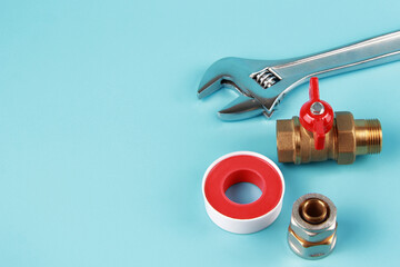 New adjustable adjustable steel key and brass water tap with adapter and sealing tape on blue background. The concept of repair, installation and connection of plumbing or gas installations.Copyspace.