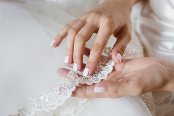 Bride's hand touching details of her wedding dress. Simple french manicure