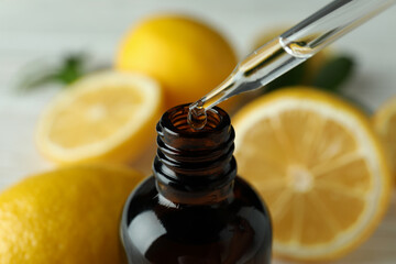 Pipette dripping oil in bottle against fresh lemons