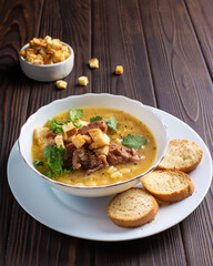 Meat soup with croutons in a white plate on a wooden table. Restaurant, menu, recipe. Close-up, front view 