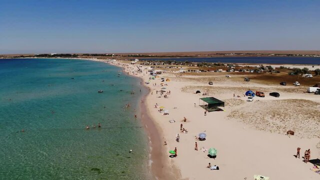 Aerial view of azure beach of central asia with tourists resting and beach umbrellas top view. Background for tourism and recreation by the sea