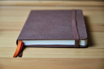 Brown notebook with an elastic band and multi-colored bookmarks on a wooden table. Selective focus. Space for lettering and design