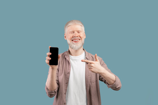 Check this app. Joyful albino guy holding and pointing finger at smartphone with black screen, studio background