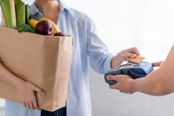 cropped view of delivery man holding payment terminal near woman with credit card on blurred background