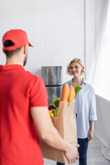 back view of arabian delivery man holding paper bag with food near smiling woman on blurred foreground