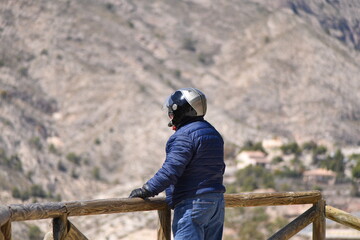 Fototapeta premium An elder man with a helmet stands at a wooden railing and looks to a scenic landscape in Spain.