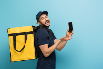 excited muslim courier laughing while pointing at smartphone on blue